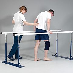Assistant helping a man with an injured knee using the remedial parallel bars, the base of the bars are dark blue, with silver adjustable inserts and white handrail.
